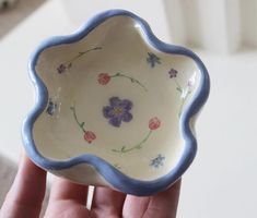 a hand holding a small bowl with flowers painted on the bottom and blue trim around the edge