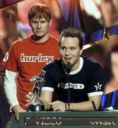 two young men standing next to each other on stage with an award in front of them