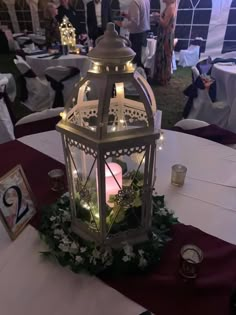 a lantern with flowers and greenery on the table at a wedding or other function