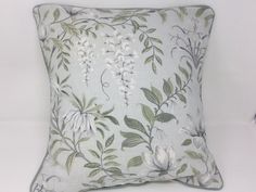 a pillow with white flowers and green leaves on the front is sitting on a table