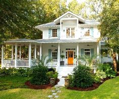 a white house with lots of trees and bushes around it's front porch area