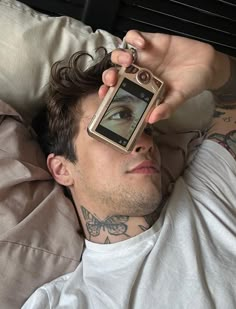 a man laying in bed holding up a cell phone to his eye