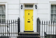 a bright yellow door sits in front of a white building with black wrought iron fence