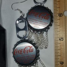 two coca cola bottle caps with chains hanging from them, next to a measuring ruler