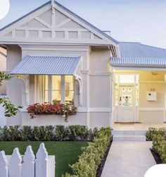 a white house with a picket fence in front of it and flowers on the window sill