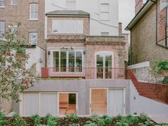 a house with two stories and a balcony on the second floor is surrounded by brick buildings