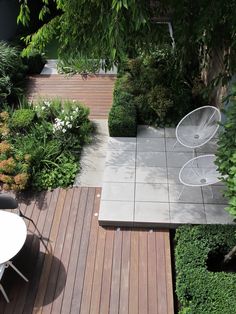 an aerial view of a wooden deck with chairs and table in the middle, surrounded by greenery