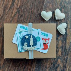 an open gift box on a wooden table with two small felt animals and three tags attached to it