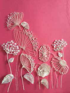 some white flowers and leaves on a pink background with beaded wire work in the middle