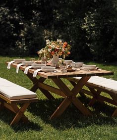 a wooden table with two benches and flowers on it in the middle of some grass