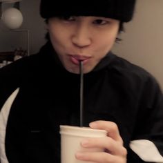 a young man drinking from a cup with a straw in his mouth while wearing a beanie