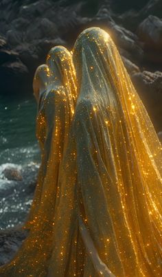 two women dressed in yellow are standing near the water with glowing veils on their heads