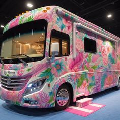 a pink floral bus is parked in a showroom with blue carpet and white walls