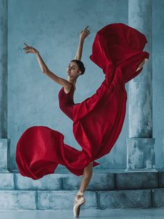 a woman in a red dress is dancing on some steps with her arms spread out