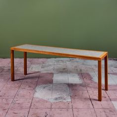 a wooden table sitting on top of a tiled floor next to a green painted wall