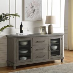 a sideboard with plates and wine glasses on it in front of a wall painting