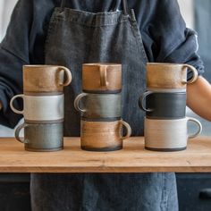 three coffee mugs sitting on top of a wooden table next to a person wearing an apron