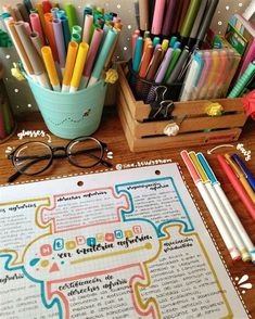 there are many pens and pencils on the table next to a book with writing in it