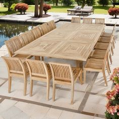 a large wooden table and chairs in front of a pool with flowers on the side