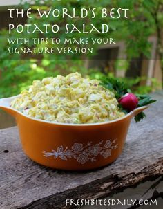 a bowl filled with potato salad sitting on top of a wooden table next to trees