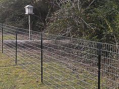 a fence with a bird feeder on top of it next to some trees and bushes