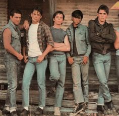 the young men are posing together in front of an old wooden building with their arms crossed