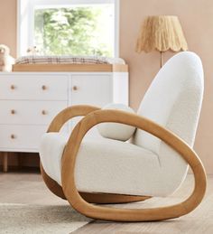 a white rocking chair with wooden arms in a living room next to a dresser and window