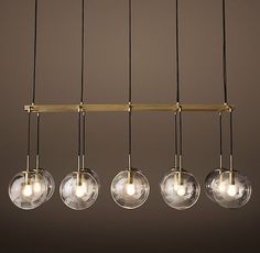 five clear glass globe lights hanging from a brass frame