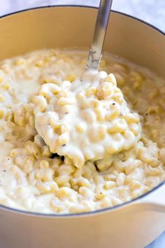 a ladle full of macaroni and cheese being stirred with a spoon in a pot