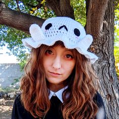 a girl wearing a knitted hat with a ghost on it's head, standing in front of a tree