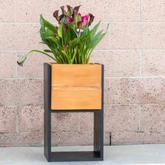 a wooden planter sitting on top of a sidewalk next to a brick wall with flowers in it