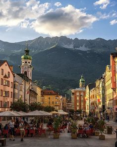 people are sitting at tables in the middle of an old town with mountains in the background