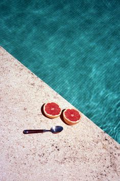 two pieces of fruit sitting on the edge of a swimming pool next to a spoon