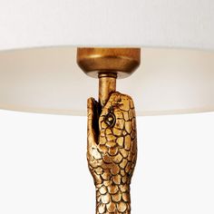 a table lamp with a gold colored snake on it's arm and a white shade