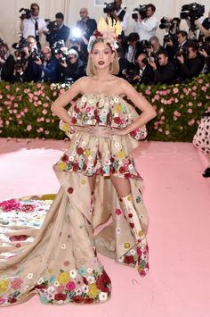 a woman in a dress with flowers on it and people taking pictures behind her at the same time