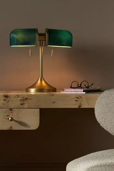 a table with a lamp and some books on it next to a chair in front of a wall