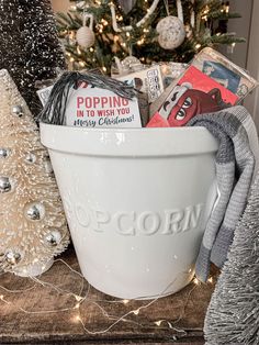 a white bucket filled with christmas items on top of a table next to a christmas tree