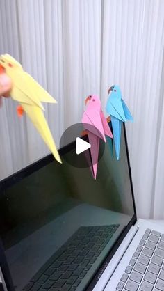 two origami birds are on the screen of a laptop computer and someone is holding one