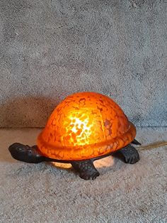 an orange turtle lamp sitting on the floor next to a gray wall and carpeted area