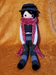 a knitted doll wearing a hat and scarf on a brown background with orange fabric