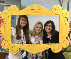 three women are posing for a picture in front of a yellow frame with an ornate design on it