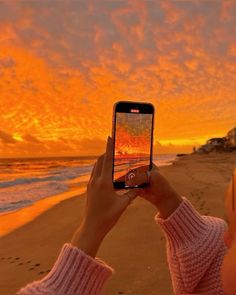 a person holding up a cell phone to take a photo on the beach at sunset