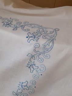 an embroidered white shirt with blue designs on the front and back, sitting on top of a bed