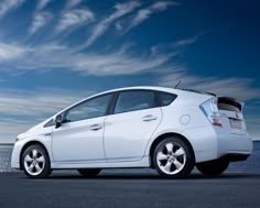 a white car is parked on the side of the road near the water and clouds