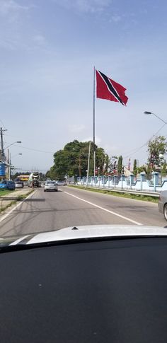 a red and white flag is flying on the side of a road with cars driving down it