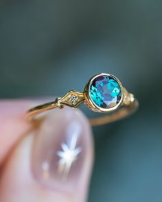 a close up of a person's hand holding a ring with a blue stone