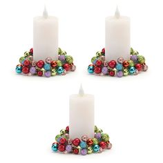 three white candles with christmas decorations around them