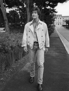 black and white photograph of man walking down the street in front of some trees with his hands in his pockets