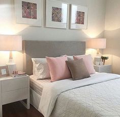 a white bed with pink pillows and two framed pictures on the wall