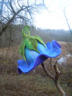 a blue and green bird bath sitting on top of a tree branch in the woods